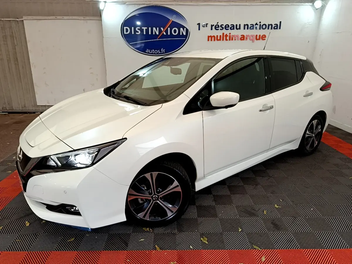 Nissan Leaf blanche vue en 3/4 avant droit dans un showroom avec logo Distinxion en arrière-plan.