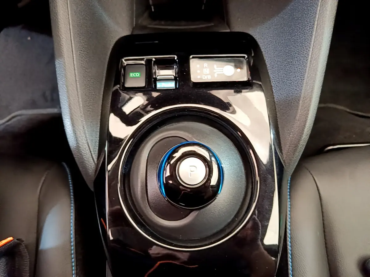 Gros plan sur la commande de boîte automatique noire avec bouton de stationnement bleu dans l'habitacle du Nissan Leaf blanc.