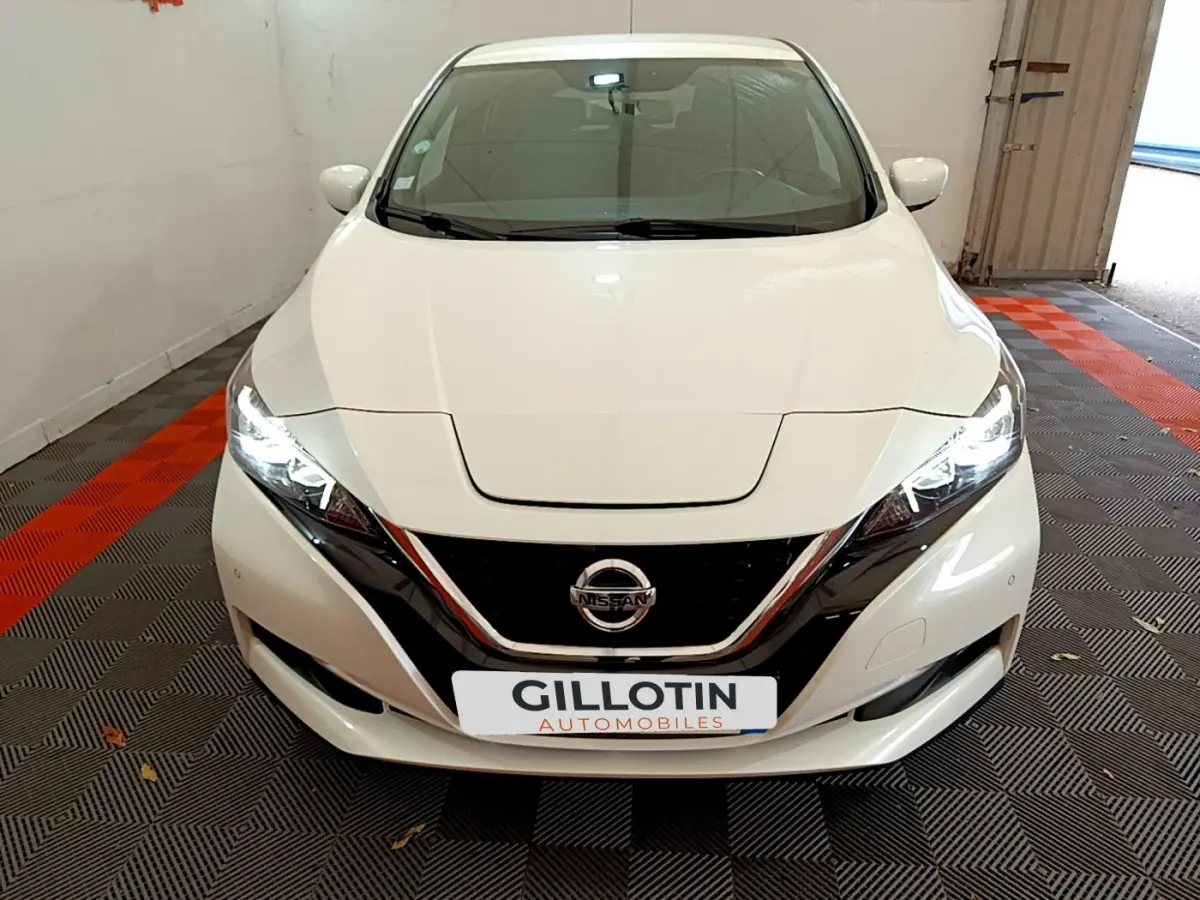 Vue avant d'une Nissan LEAF blanche 2020 avec phares LED allumés et calandre noire brillante.