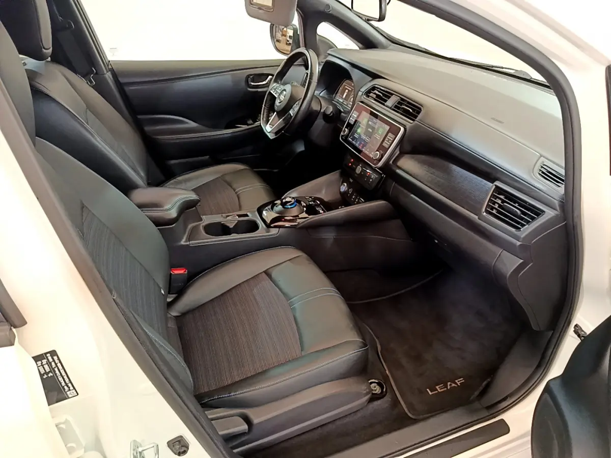 Intérieur avant droit du Nissan Leaf blanc 2020, sièges noirs, tableau de bord avec écran tactile et volant cuir.