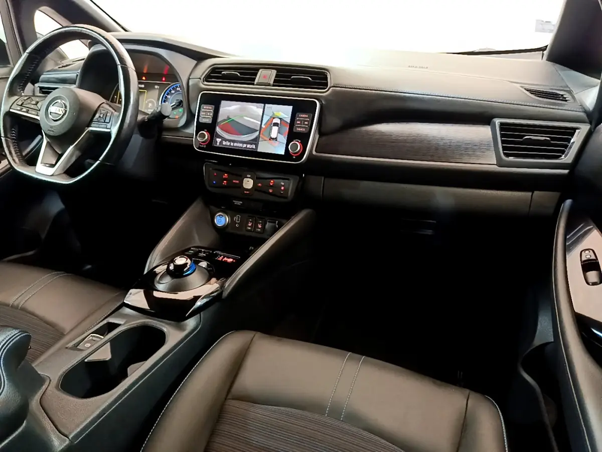 Vue intérieure avant du tableau de bord et volant cuir noir du Nissan Leaf blanc avec écran tactile et commandes au volant.