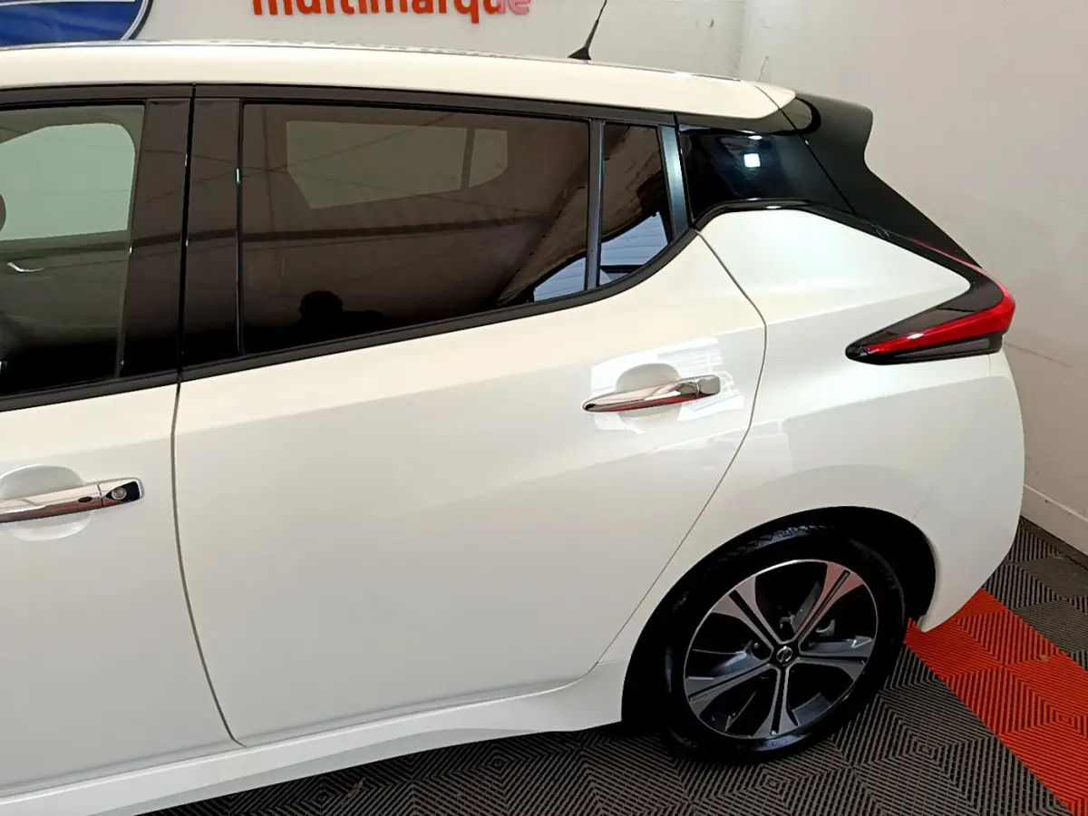 Vue côté droit arrière d'une Nissan Leaf blanche avec toit noir et feux arrière profilés en intérieur showroom.