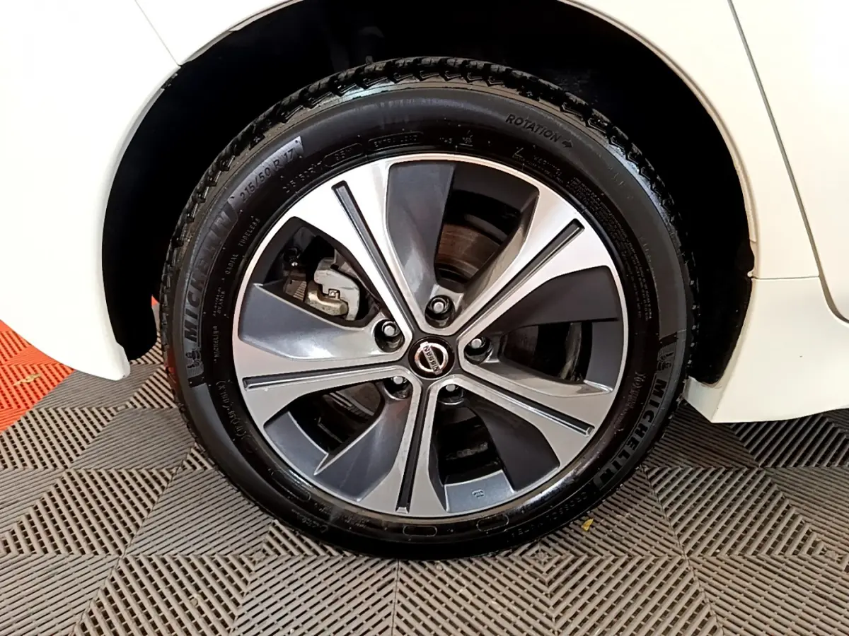 Gros plan sur la roue avant droite d'une Nissan Leaf blanche avec jante alliage bicolore et logo Nissan au centre.