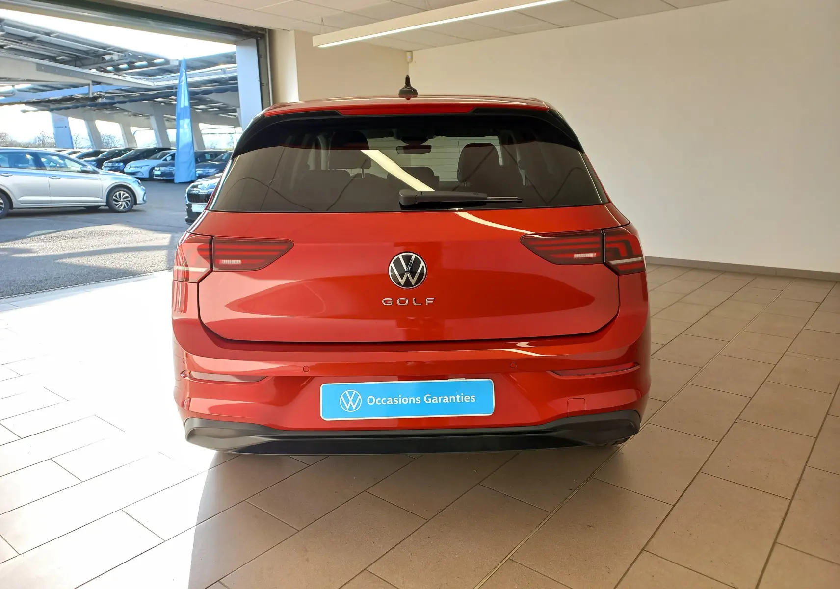 Vue arrière d'une Volkswagen Golf 2.0 TDI 150 DSG7 Style rouge métallisé, stationnée en intérieur lumineux.