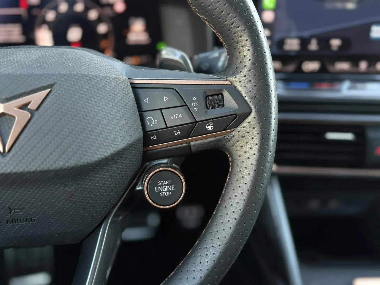 Gros plan sur le volant perforé noir de la CUPRA Leon 2025 avec bouton Start Engine Stop et commandes intégrées.