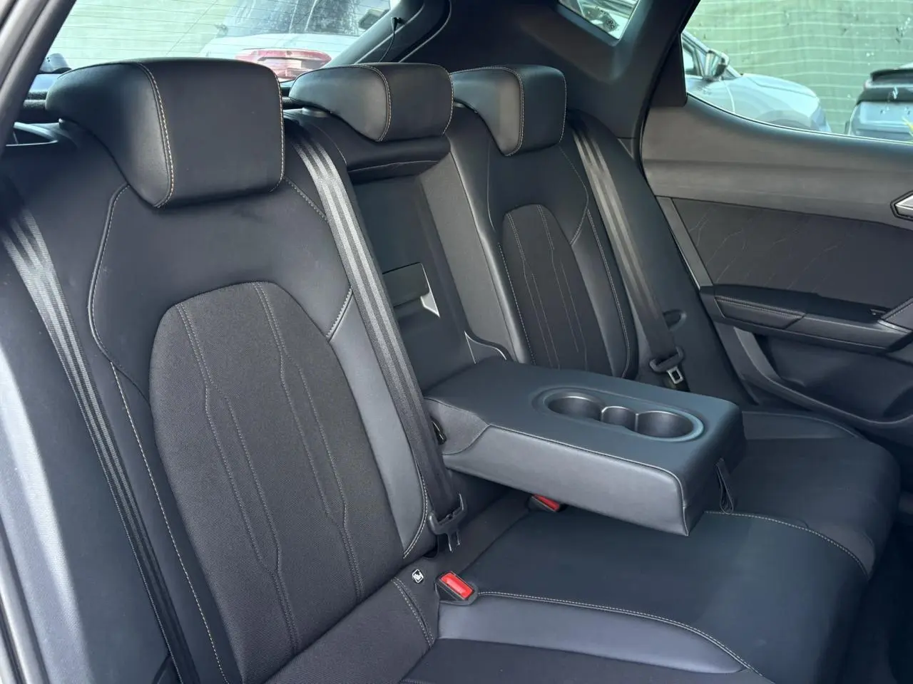 Vue intérieure des sièges arrière noirs avec accoudoir central rabattable et ceintures de sécurité visibles dans une CUPRA Leon 2025.