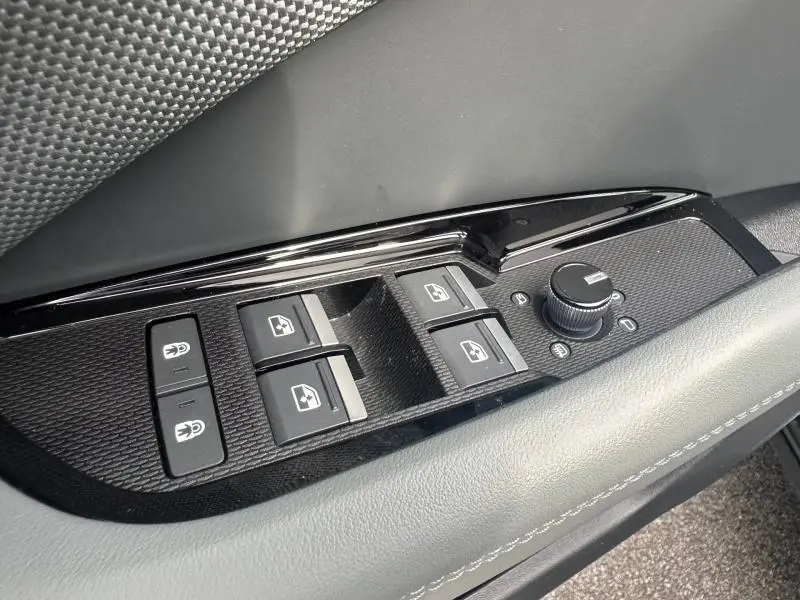 Gros plan sur les commandes de lève-vitres et réglage des rétroviseurs côté conducteur d’un Audi Q3 gris 2026.