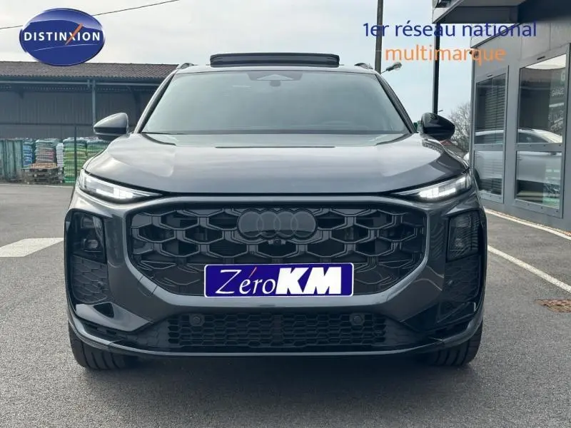 Vue frontale d'un Audi Q3 gris 2026 avec calandre noire hexagonale et phares LED fins allumés.