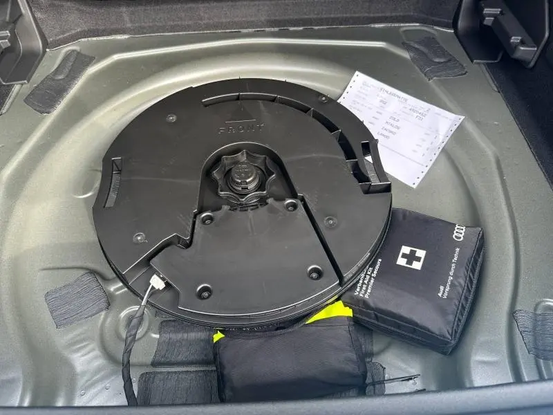 Vue rapprochée du coffre d'un Audi Q3 gris 2026, montrant la roue de secours et une trousse de premiers secours.