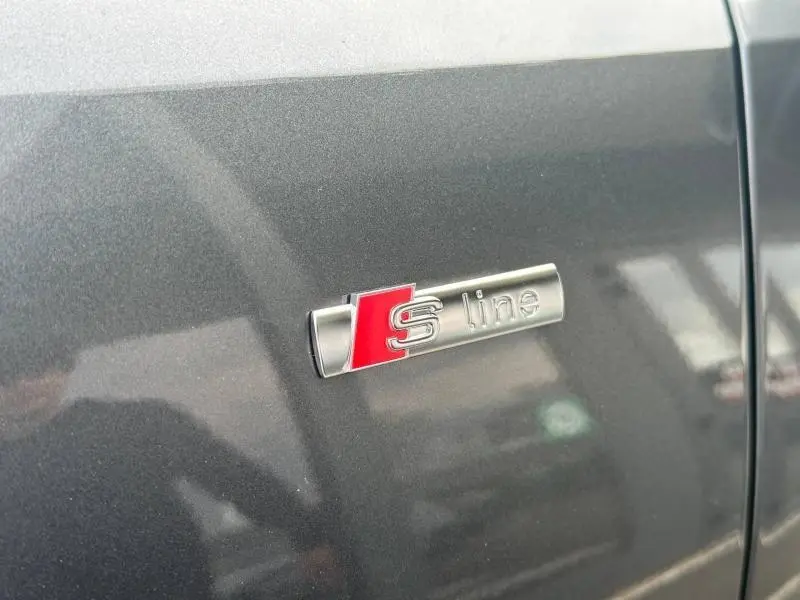 Gros plan sur l'emblème S line argent et rouge sur la porte gris métallisé d'un Audi Q3 2.0 TDI 2026.