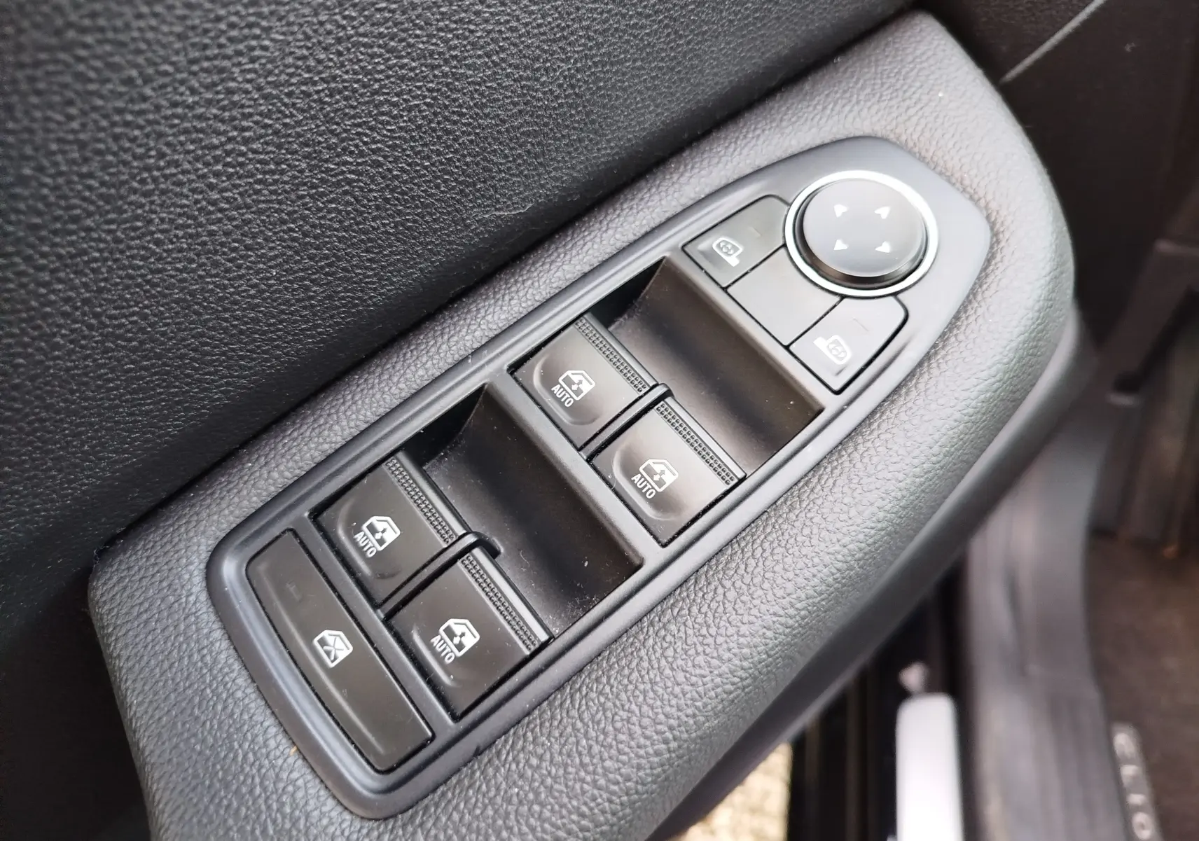 Gros plan sur les commandes de lève-vitres et réglage des rétroviseurs côté conducteur d’une Renault Clio noir étoile.