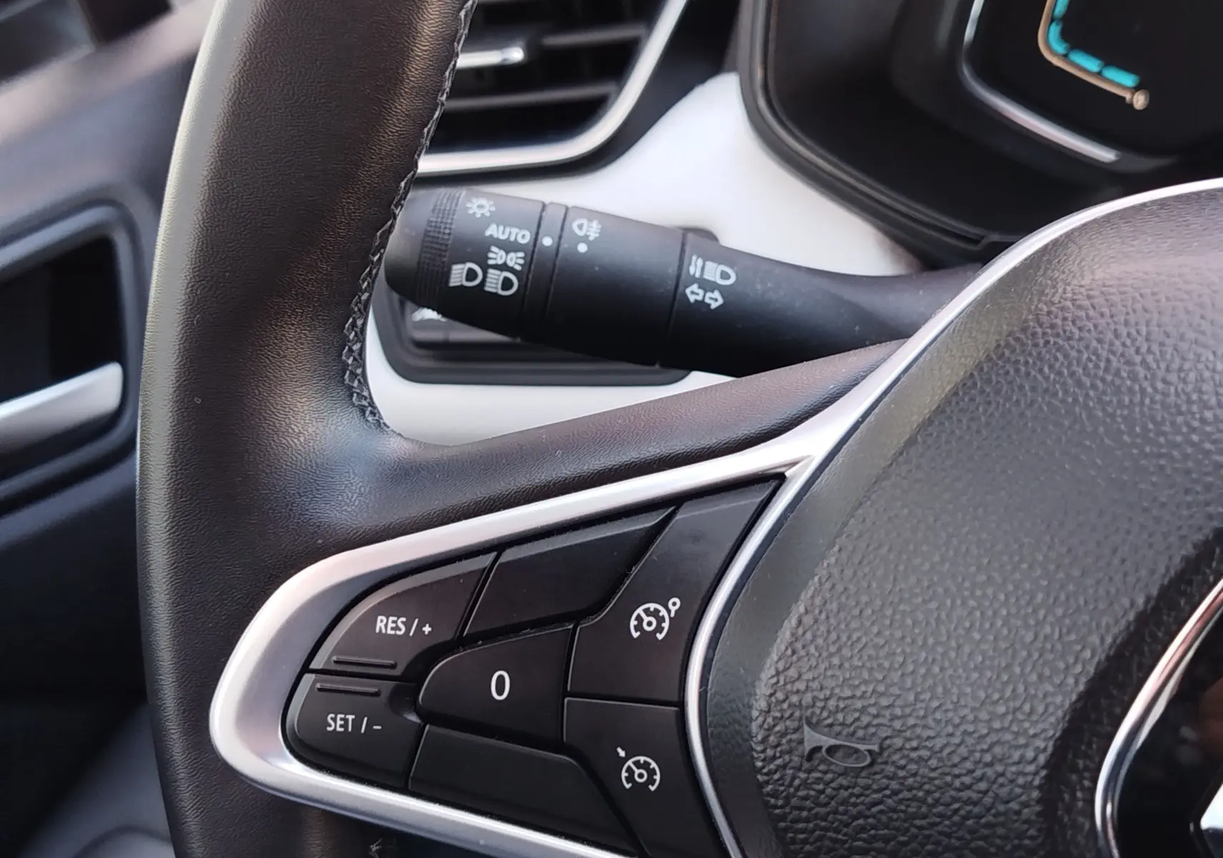 Gros plan sur le volant noir de la Renault Clio 1.6 E-Tech 2022, avec commandes de régulateur de vitesse et commodo d'éclairage.