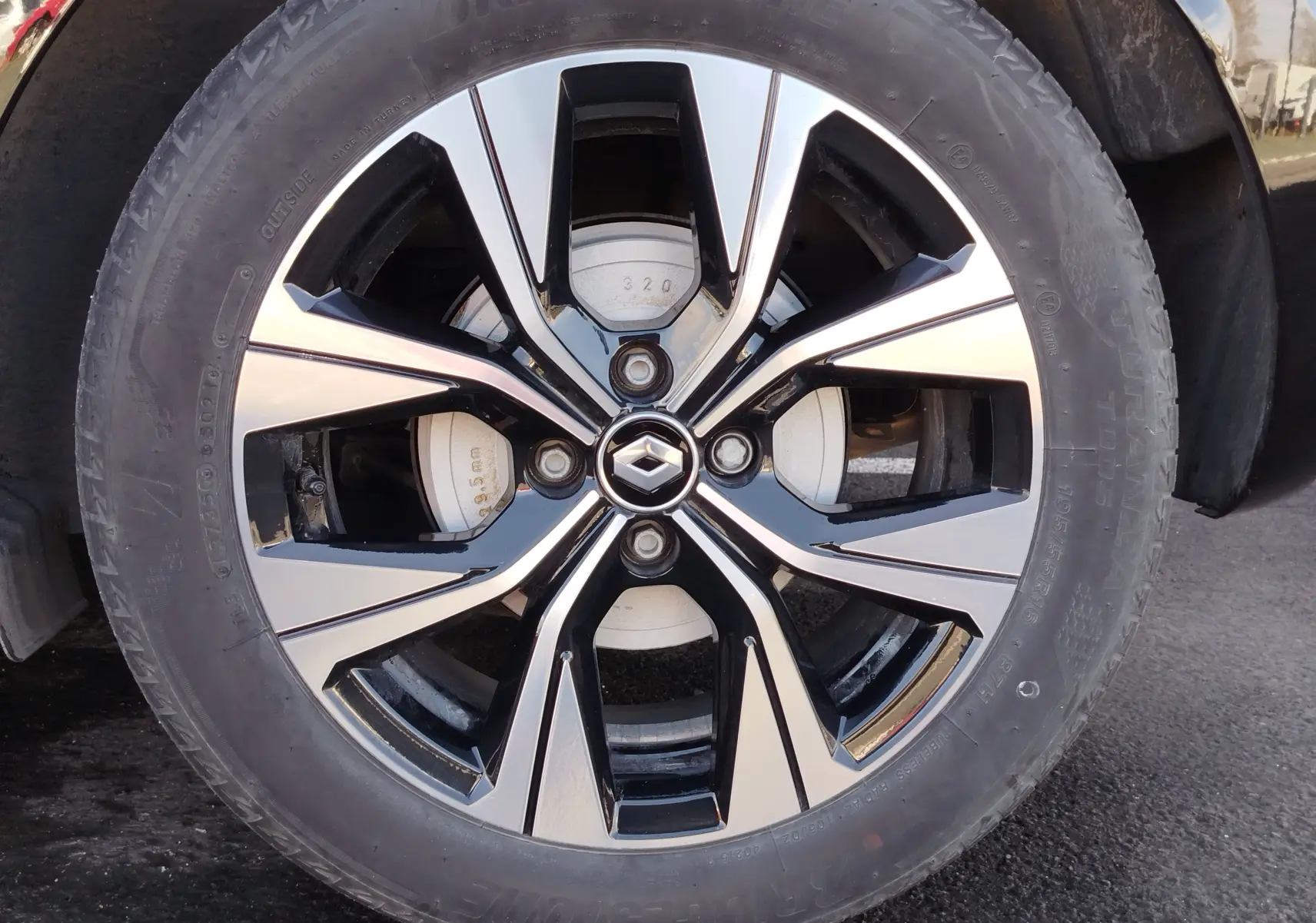 Gros plan sur la jante alliage bicolore noire et argent avec logo Renault au centre, roue avant droite du Renault Clio noir étoile.