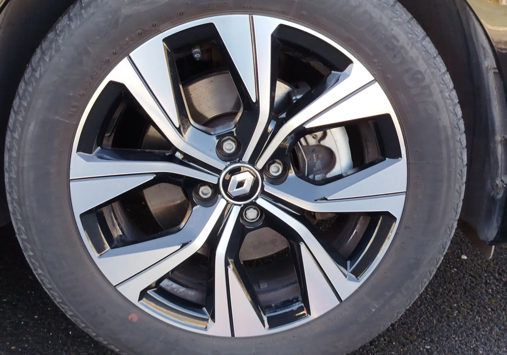 Gros plan sur la jante alliage bicolore noire et argent avec logo Renault au centre, roue d'une Clio 1.6 E-Tech noir étoile.