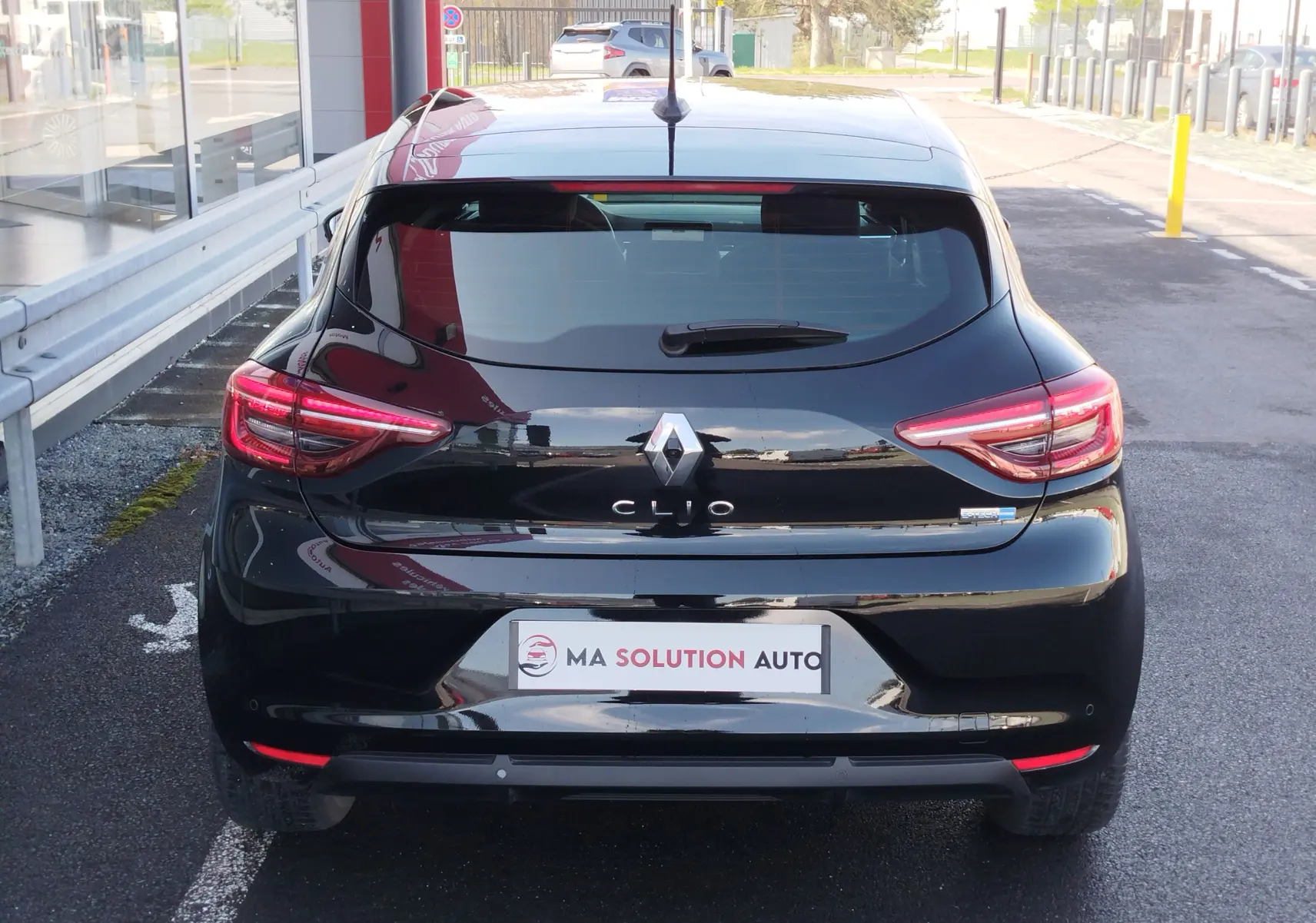Vue arrière d'une Renault Clio 1.6 E-Tech noir étoile, avec feux LED allumés et logo Renault bien visible.