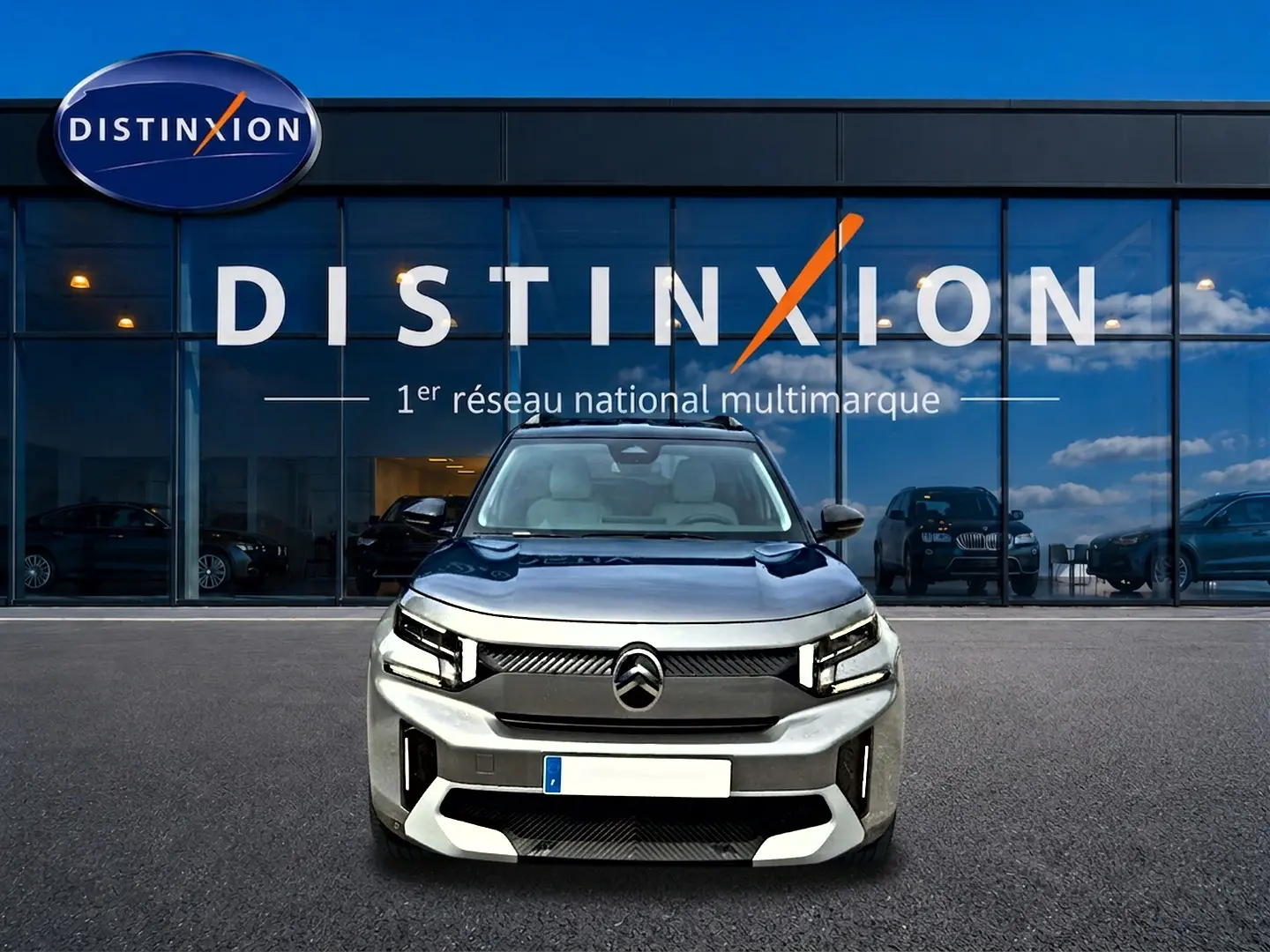 Vue de face d'une Citroën C3 Aircross gris mercury, avec calandre noire et phares LED, devant une vitrine Distinxion.