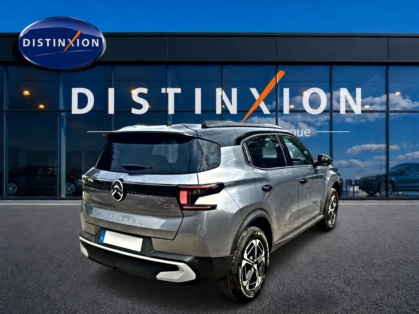 Vue 3/4 arrière droite d'un Citroën C3 Aircross gris mercury avec jantes alu et toit noir devant un bâtiment Distinxion.
