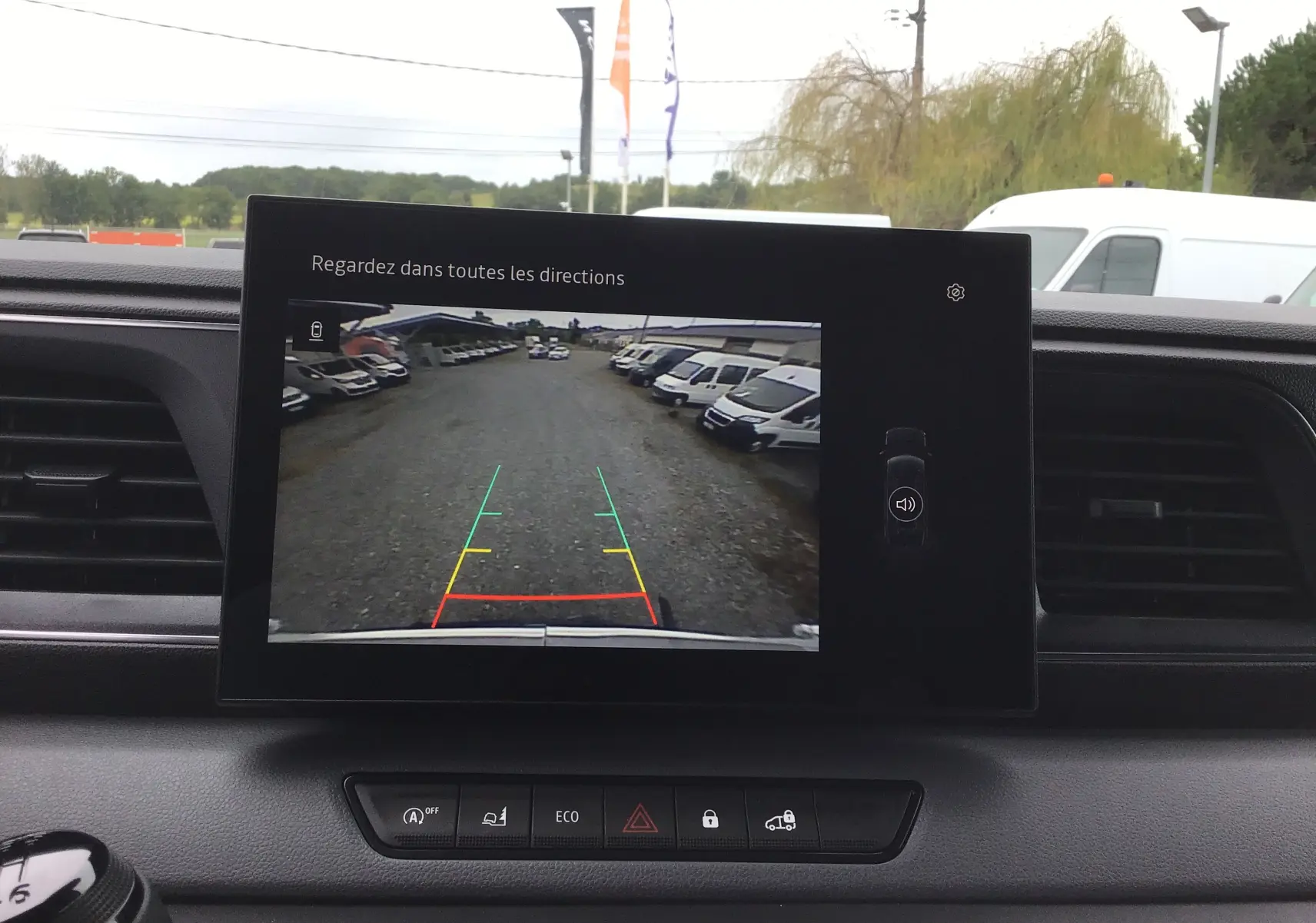 Vue depuis l'intérieur du Renault Master blanc 2025, écran multimédia affichant la caméra de recul avec vue sur un parking de véhicules blancs.