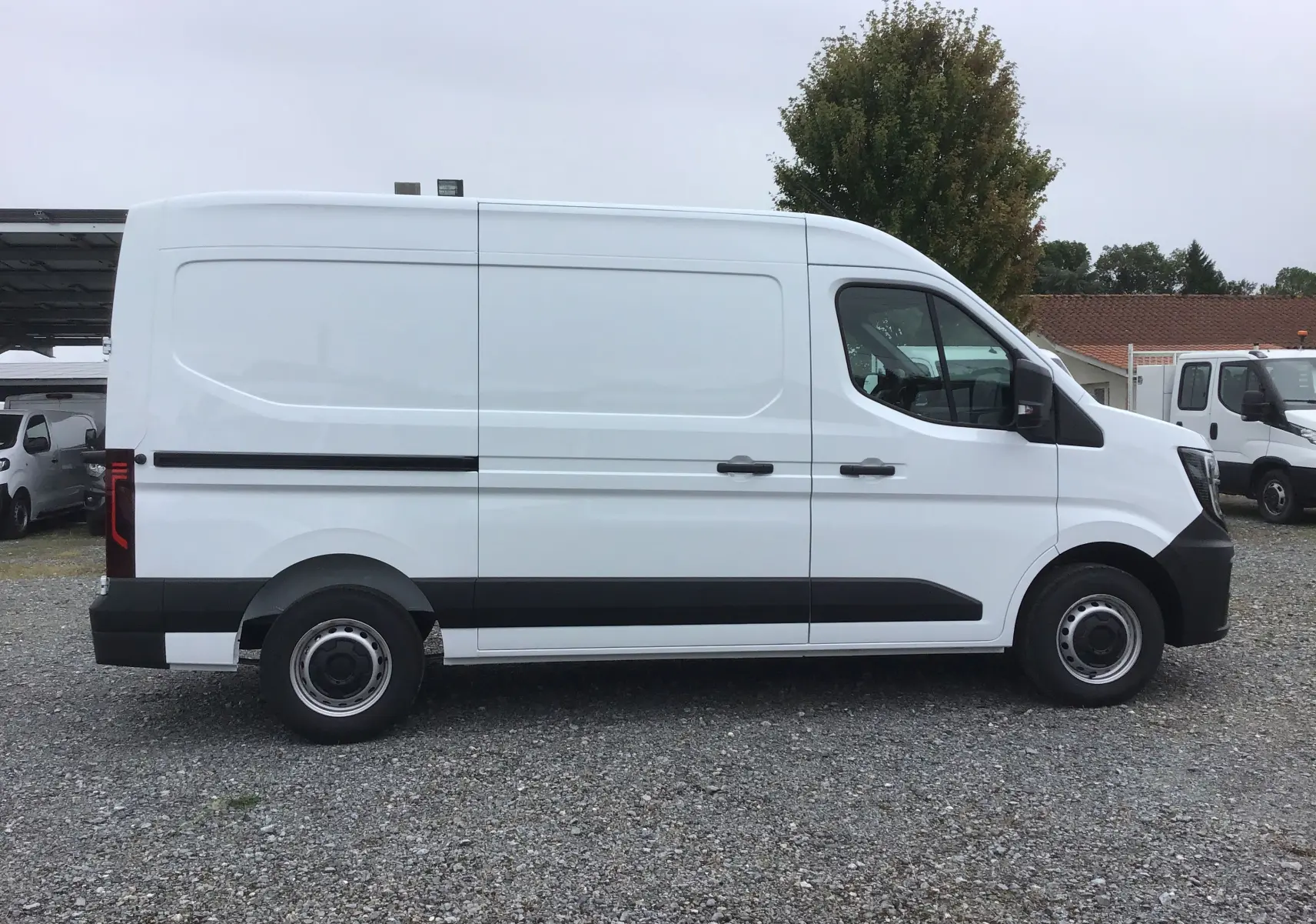 Profil côté gauche du fourgon blanc Renault Master L2H2 2025 avec bande noire et roues acier visibles.