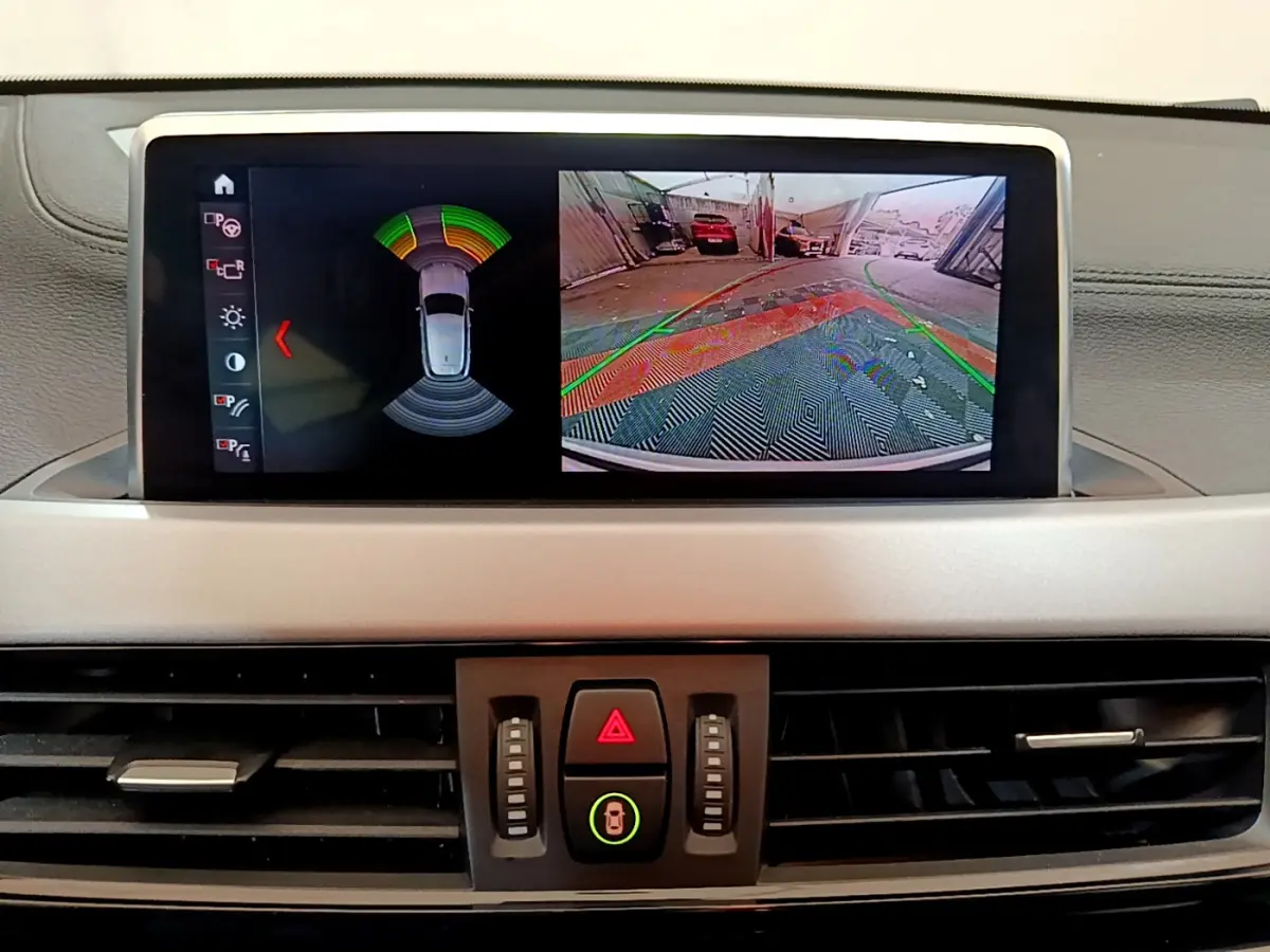 Écran central du tableau de bord du BMW X2 blanc 2023 montrant l'aide au stationnement arrière avec caméra et capteurs.