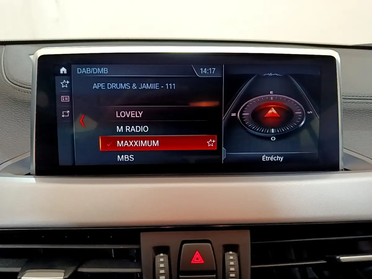 Écran central du tableau de bord du BMW X2 blanc 2023 affichant la radio et la boussole numérique.