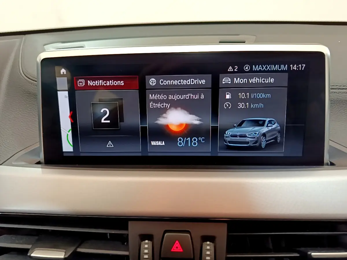 Écran central du tableau de bord BMW X2 2023 affichant météo, notifications et consommation, vue intérieure frontale.