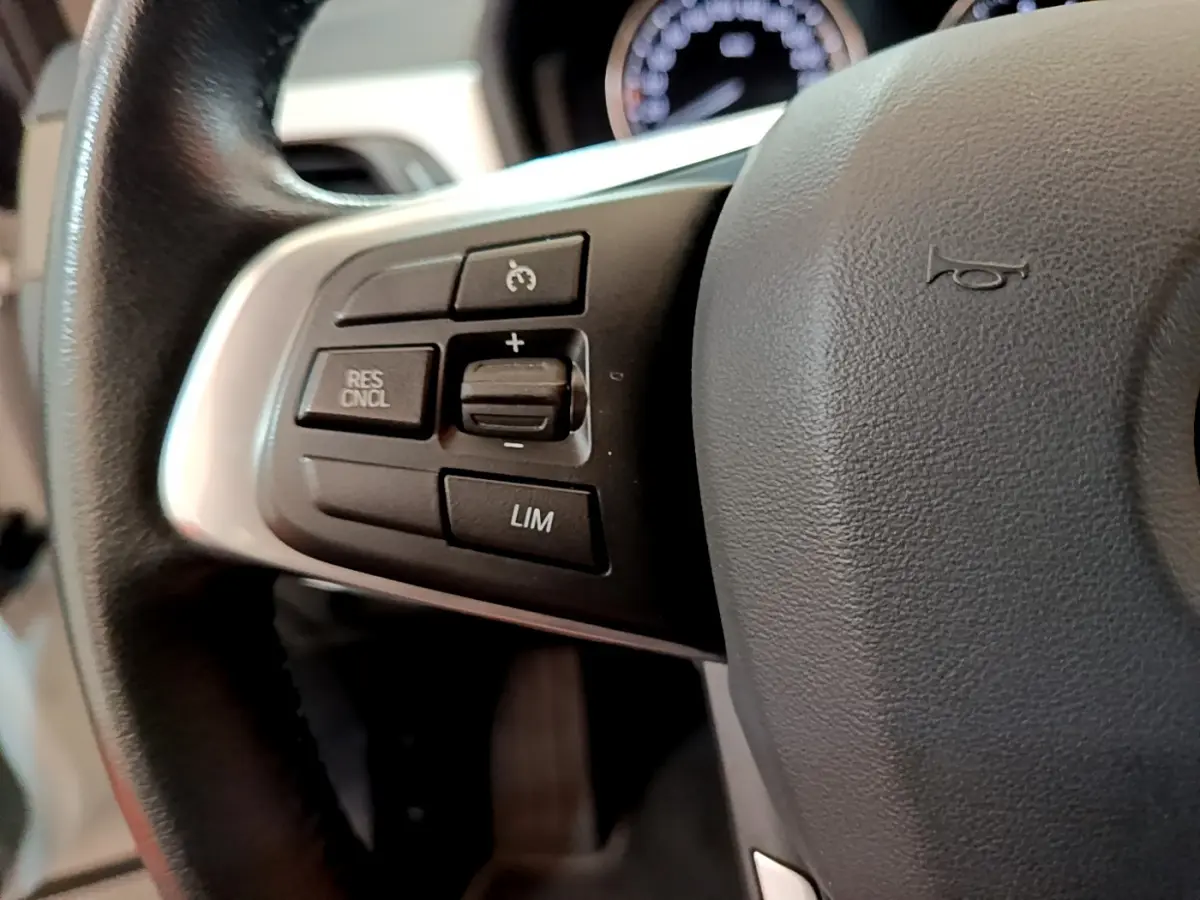 Gros plan sur les commandes du volant à gauche d'une BMW X2 blanche, avec boutons de régulateur de vitesse visibles.