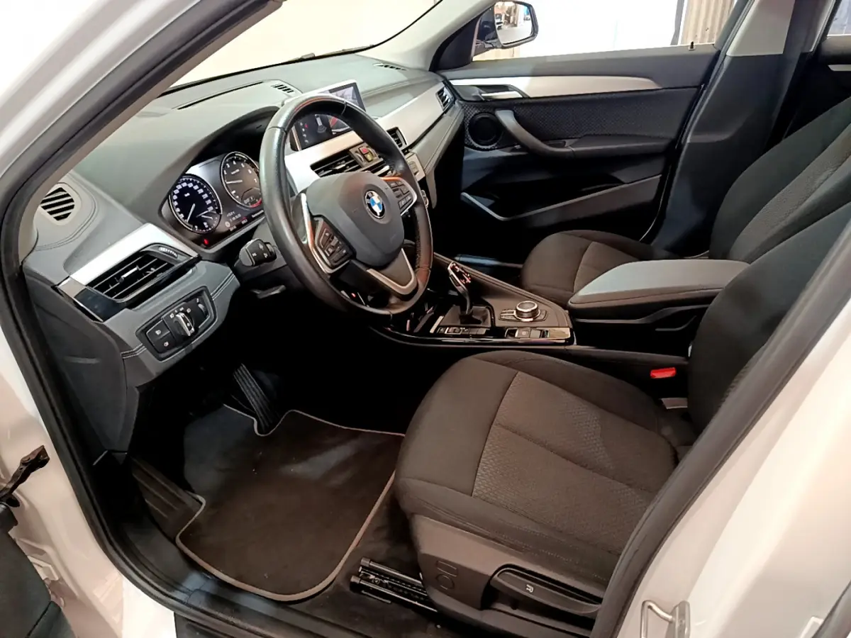 Intérieur côté conducteur de BMW X2 blanc 2023, volant cuir multifonctions et tableau de bord digital visible.