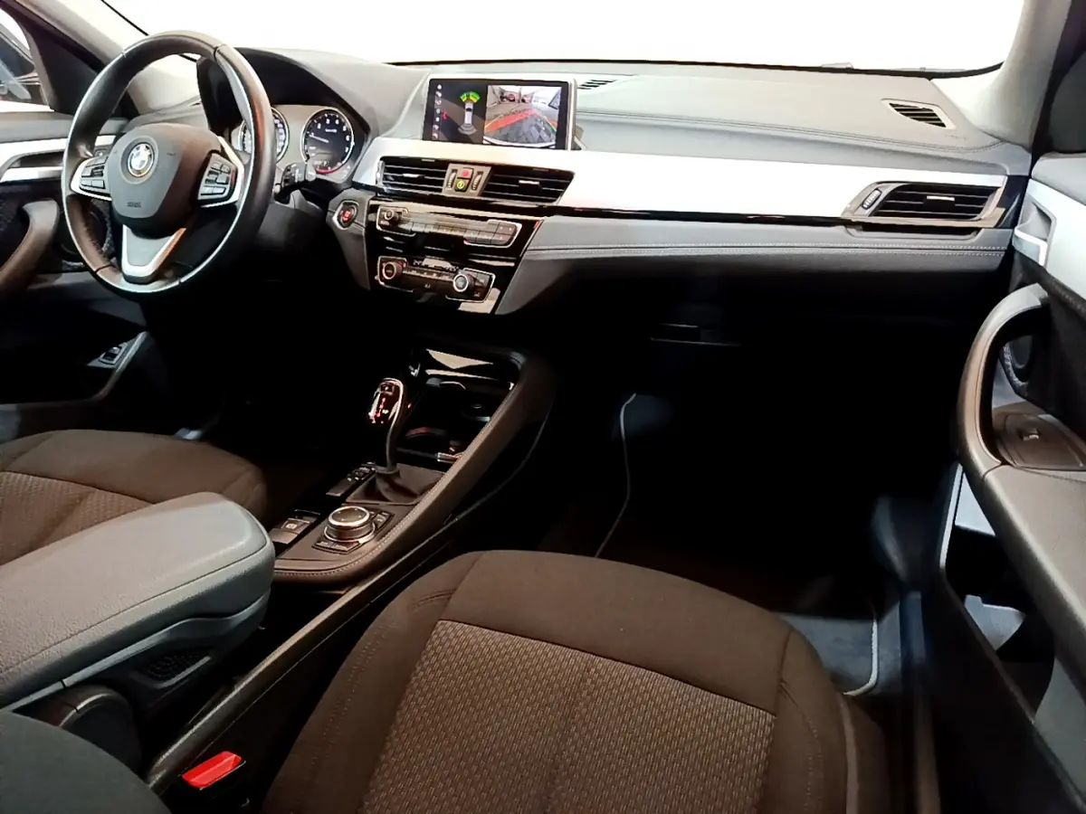 Intérieur BMW X2 sDrive18i 2023 vu côté passager, tableau de bord noir avec écran central et volant cuir multifonctions.
