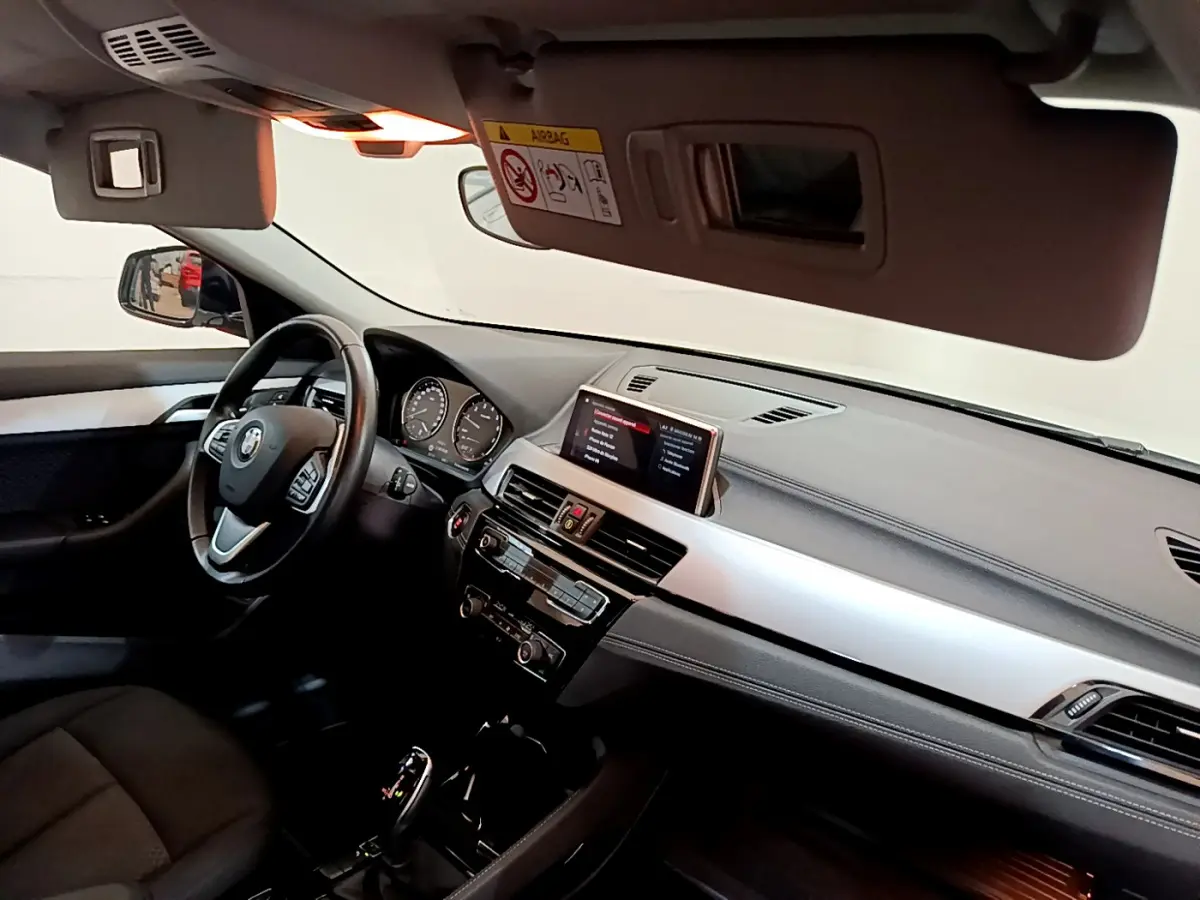 Vue intérieure côté conducteur du tableau de bord et volant cuir d'une BMW X2 sDrive18i blanc 2023.