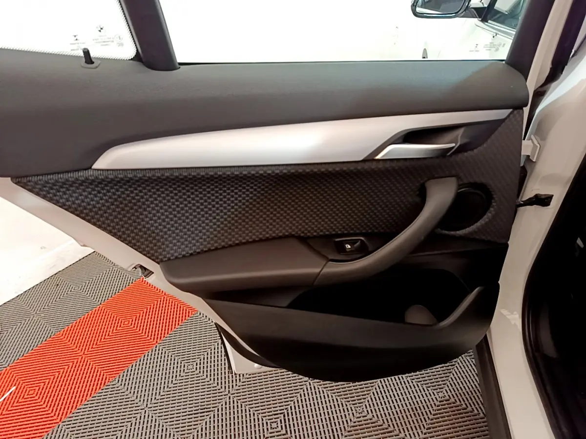 Gros plan sur la porte avant droite blanche d'une BMW X2 2023, avec habillage noir texturé et poignée intégrée.