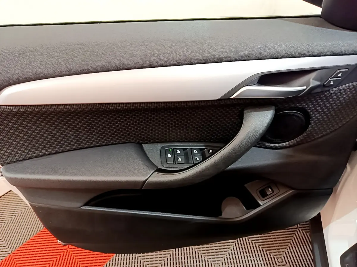 Gros plan sur la porte côté gauche de la BMW X2 blanche, montrant les commandes de vitres et la poignée intérieure noire.
