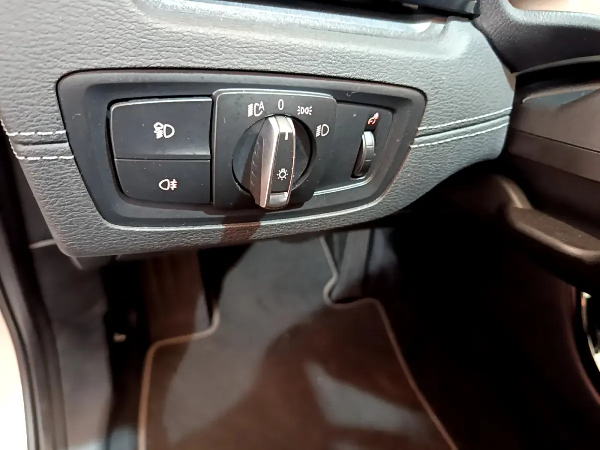 Gros plan sur le bouton de commande des phares sur la gauche du tableau de bord noir du BMW X2 blanc 2023.