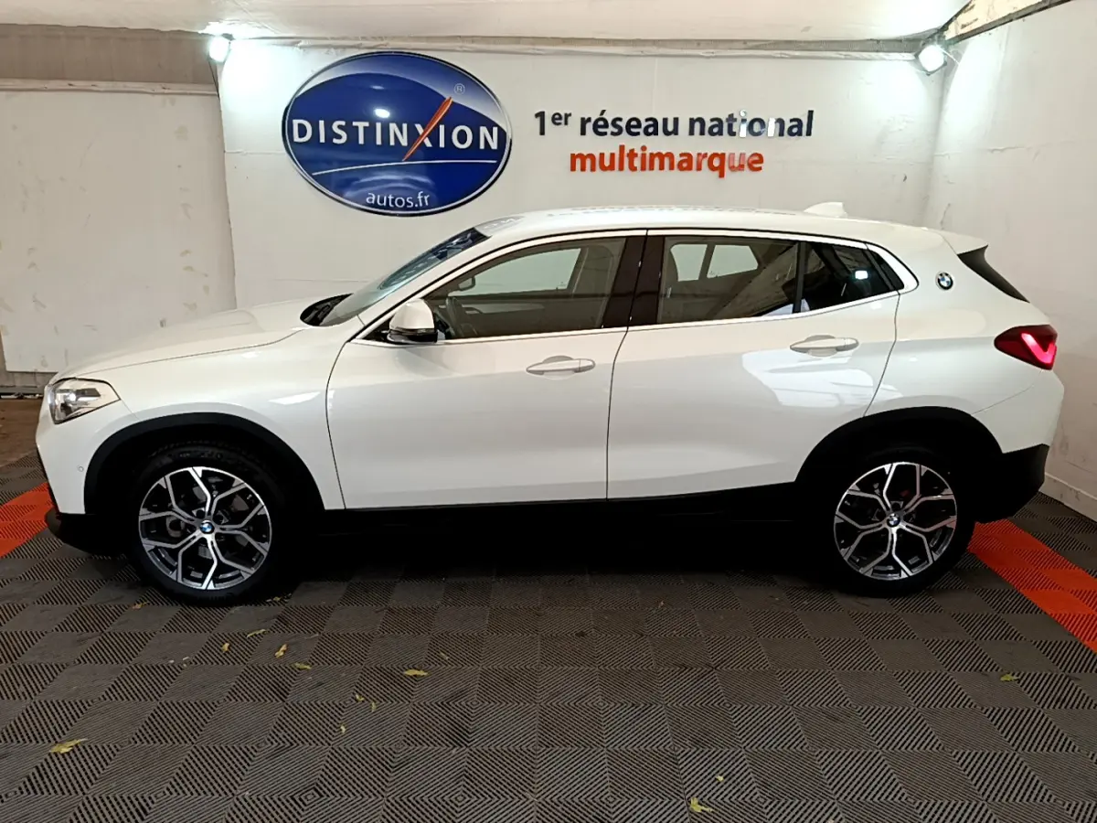 Profil côté gauche d'un BMW X2 blanc 2023 avec jantes alliage et feux arrière LED allumés en intérieur showroom