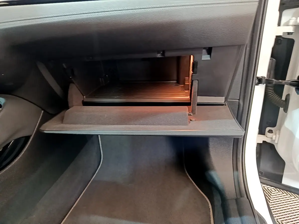 Gant de boîte à gants ouvert côté passager d'un BMW X2 blanc, montrant l'intérieur éclairé et le tapis noir.