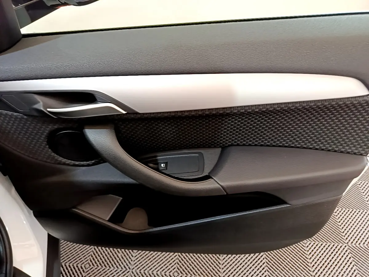 Gros plan sur la porte côté gauche intérieure du BMW X2 blanc, avec poignée et bouton de verrouillage visibles.