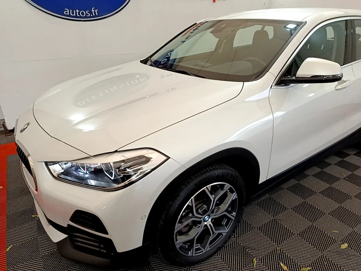 BMW X2 blanc en vue 3/4 avant droit, avec phares LED allumés et jantes alliage distinctives.