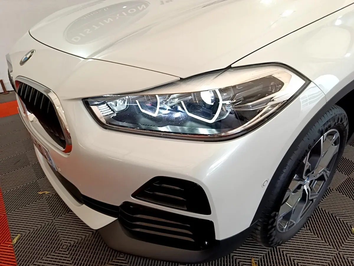 Gros plan sur l'avant droit d'un BMW X2 blanc 2023, mettant en valeur son phare LED et la calandre caractéristique.