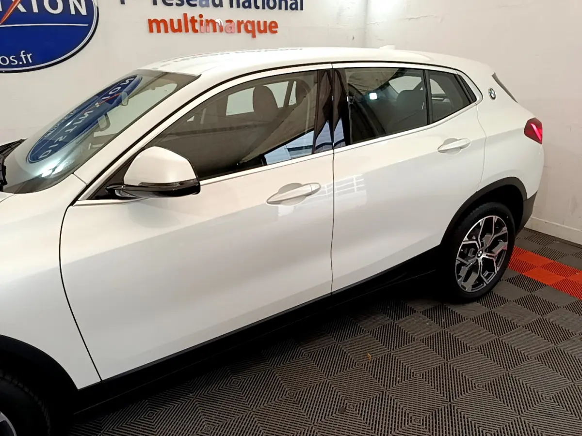 Vue latérale côté gauche d'un BMW X2 blanc 2023 avec jantes alliage et rétroviseurs blancs sur sol damier.