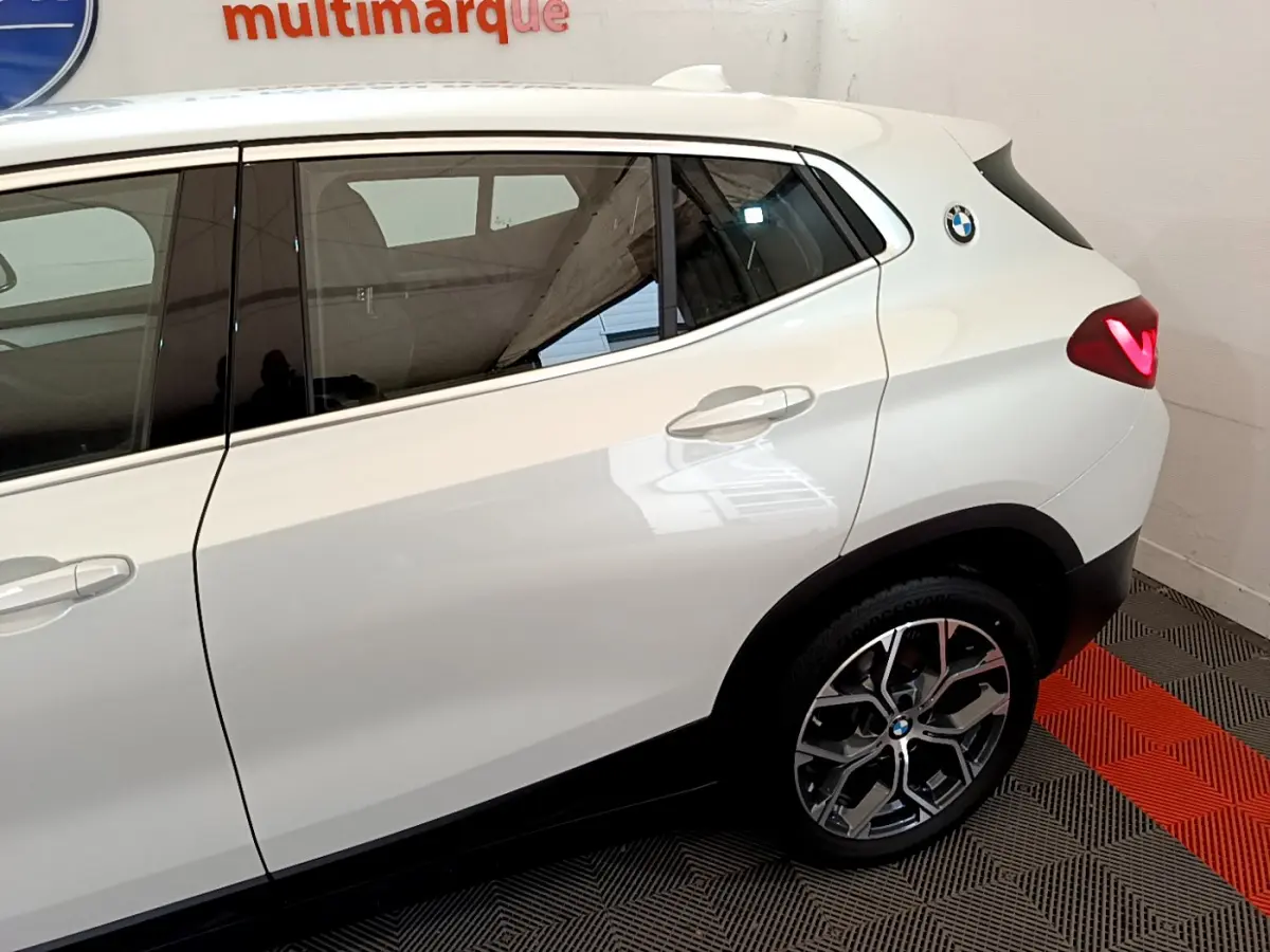 Vue latérale droite du BMW X2 blanc 2023, mettant en valeur la porte arrière, la jante alliage et le logo rond sur l'aile arrière.