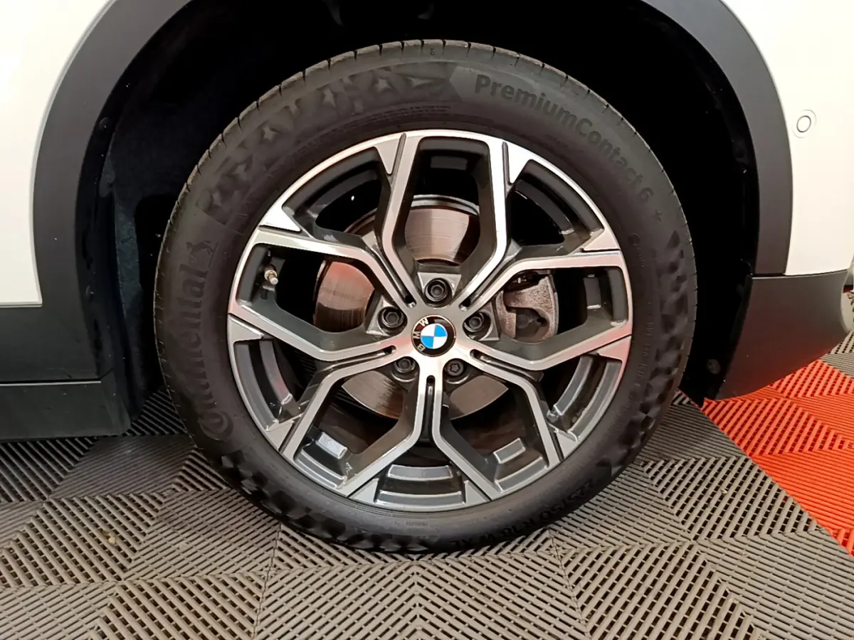 Gros plan sur la roue avant droite d'un BMW X2 blanc, avec jante alliage au design moderne et logo central visible.