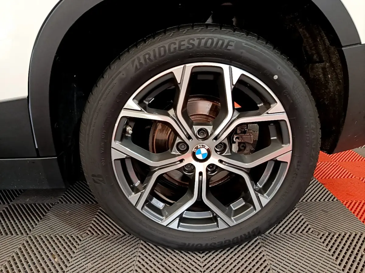 Gros plan sur la roue avant droite d'un BMW X2 blanc, mettant en valeur la jante alliage et le pneu Bridgestone.