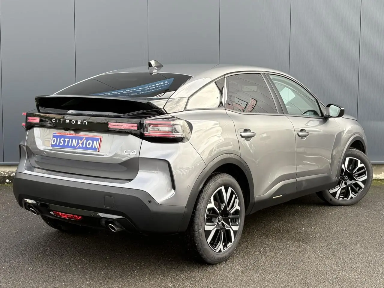 Vue 3/4 arrière droite d'une Citroën C4 Hybrid 2025 gris Mercury avec jantes alliage et toit noir brillant.