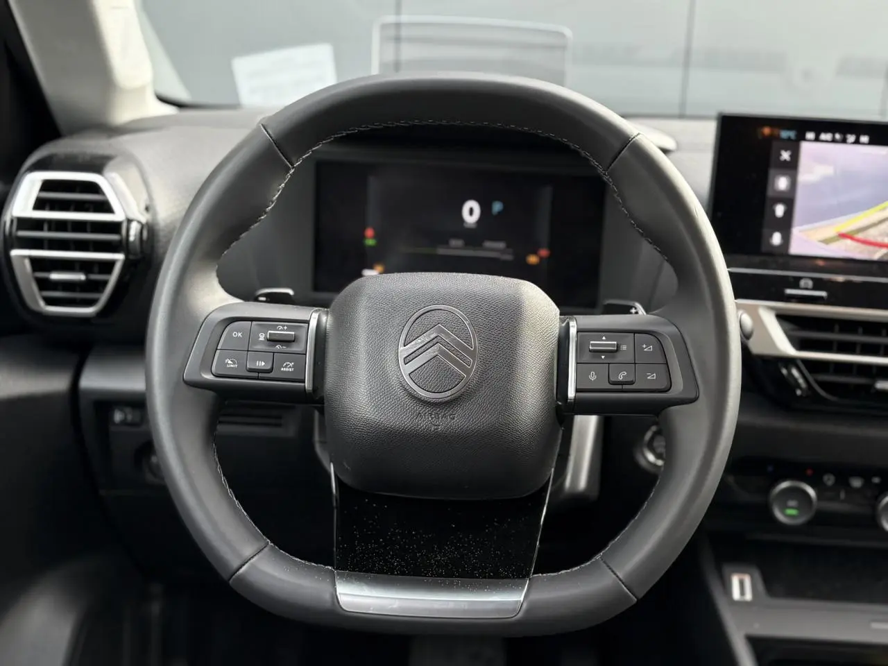 Vue rapprochée du volant cuir noir du Citroën C4 Hybrid 2025 avec commandes intégrées et tableau de bord numérique.