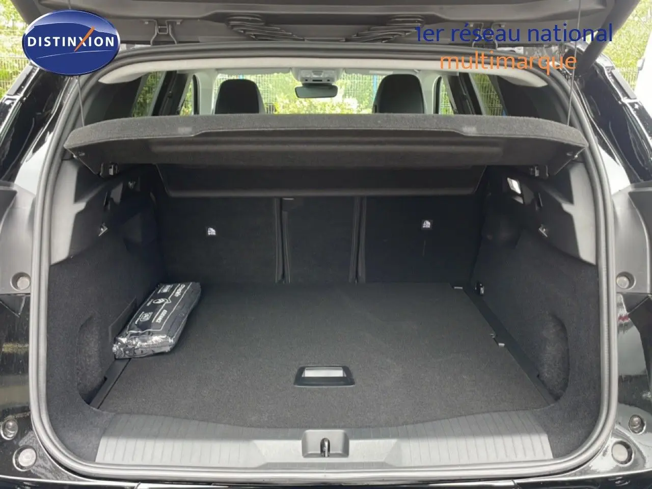 Coffre ouvert vu de l'arrière d'un Citroën C5 Aircross noir Perla Nera, avec cache-bagages et tapis noir.