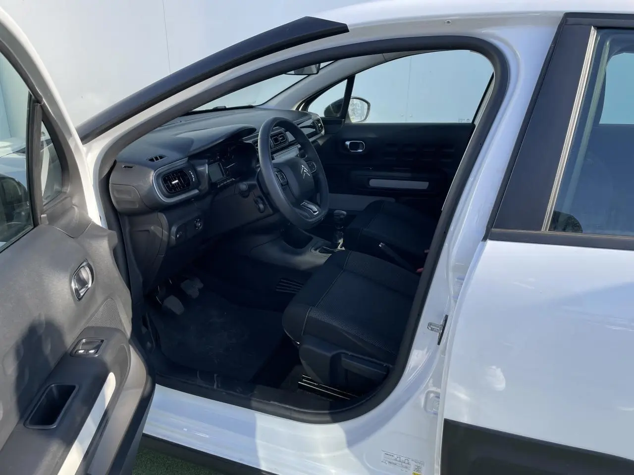 Intérieur côté conducteur d'une Citroën C3 blanc banquise 2024, montrant tableau de bord et sièges noirs.