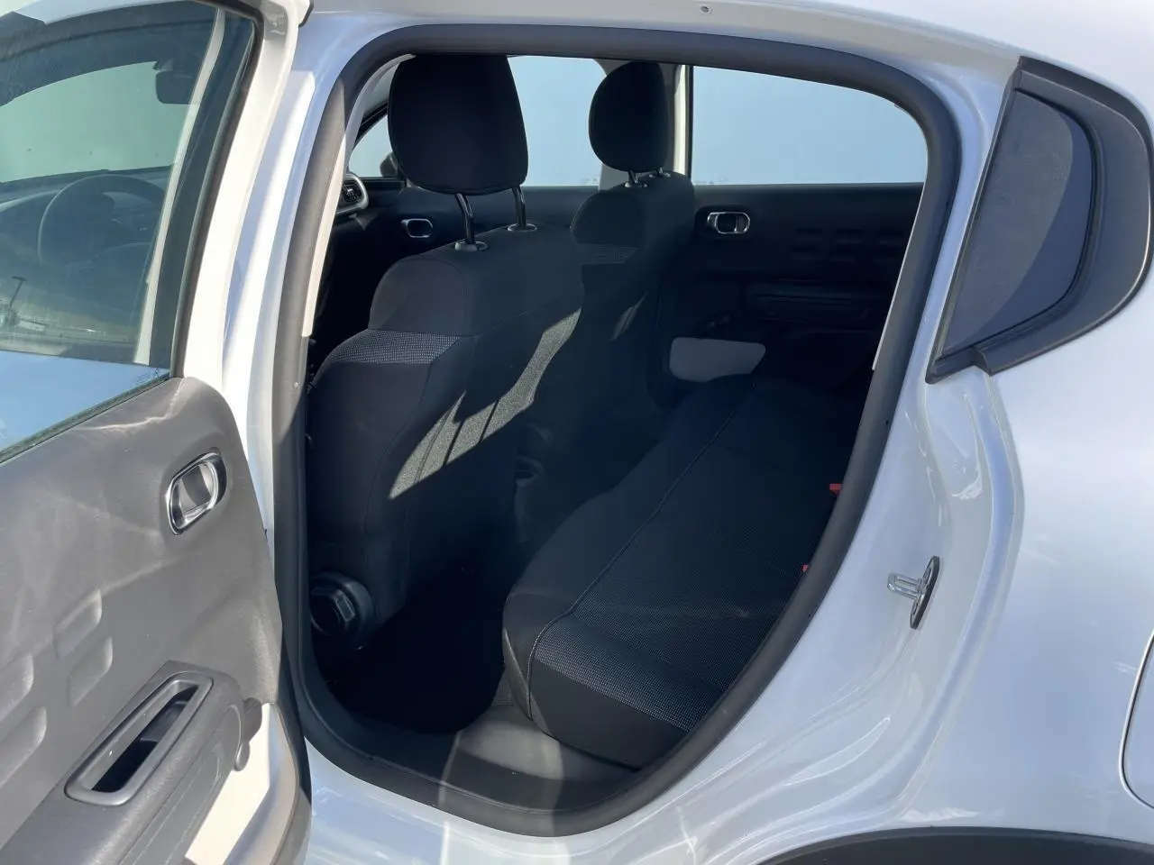 Vue intérieure côté droit de la banquette arrière noire d'une Citroën C3 blanche avec porte ouverte.