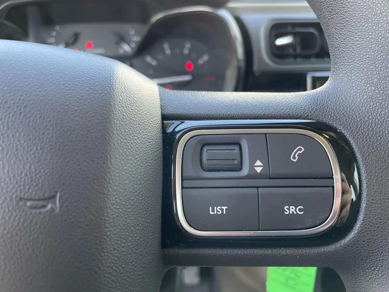 Gros plan sur les commandes audio au volant noir brillant de la Citroën C3 blanche, avec tableau de bord flou en arrière-plan.