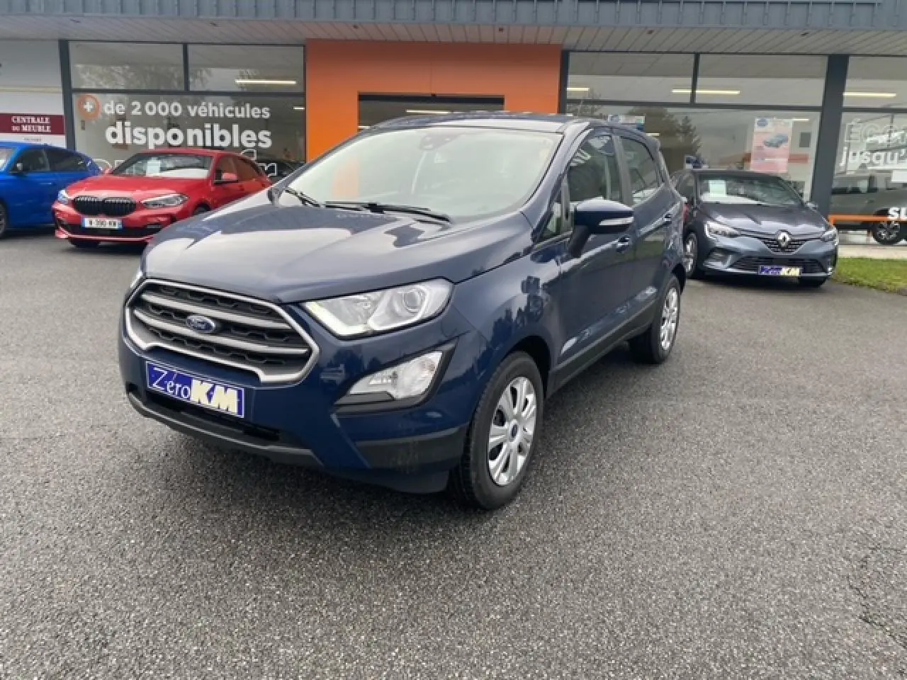 Ford EcoSport bleu abysse en 3/4 avant droit, avec calandre chromée et feux de jour LED visibles sur parking.
