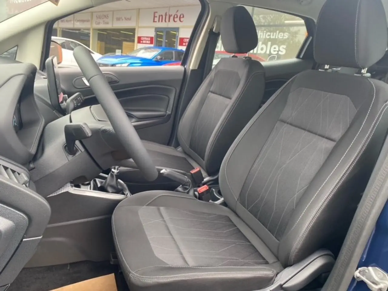 Vue intérieure côté conducteur du Ford EcoSport bleu abysse 2022, montrant les sièges avant en tissu noir et la boîte manuelle.